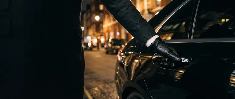 Main gantée d’un chauffeur sur la portière arrière d’une voiture de luxe